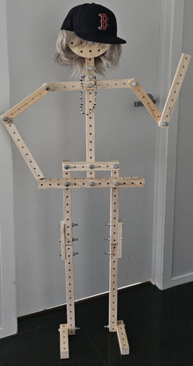 Wooden mannequin with a cap against a plain wall.