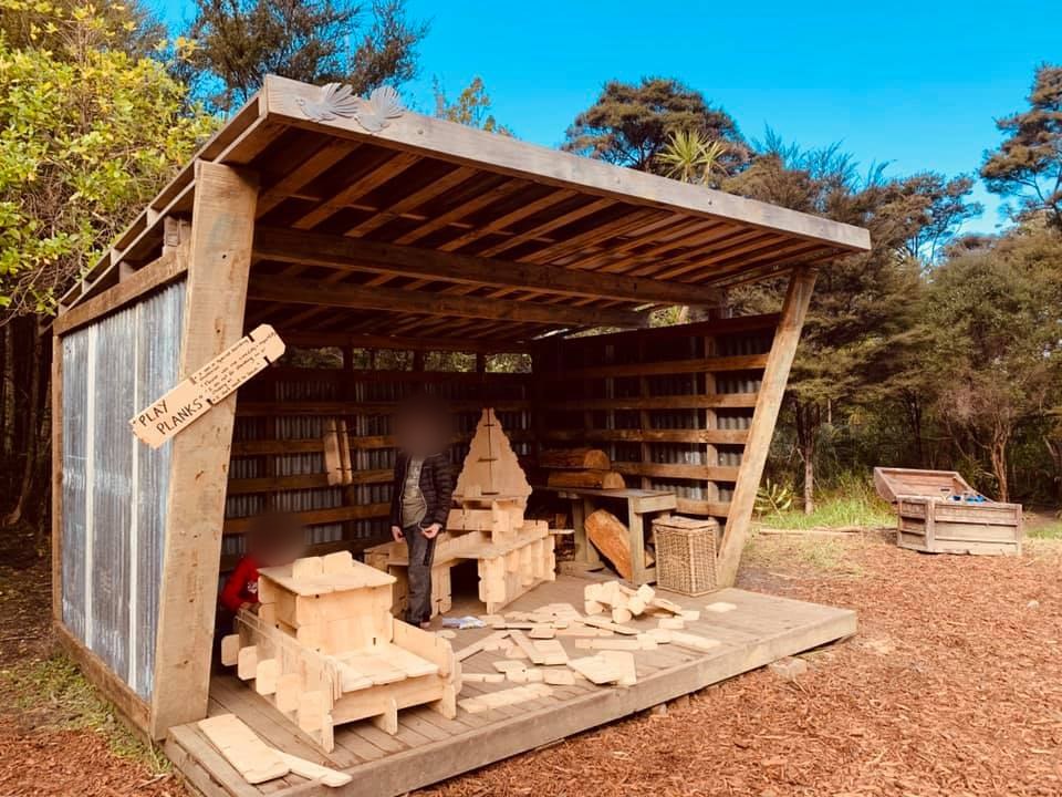 Two children building with Play Planks inside a timber forest-school shelter